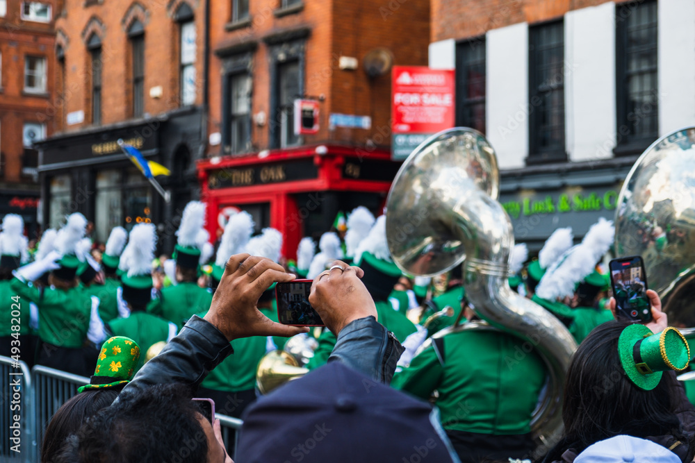 Fototapeta premium Person taking photos of the march, green hats in the crowd, the Saint Patrick's day parade in Dublin 2022, Ireland