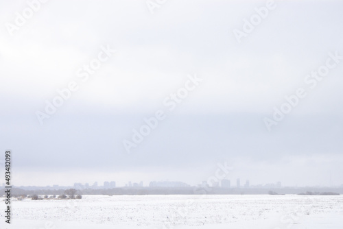The city is on the fog far away. A cloudy blue sky is on top and white snow is on the bottom of the frame. Wide landscape shot © Norgle
