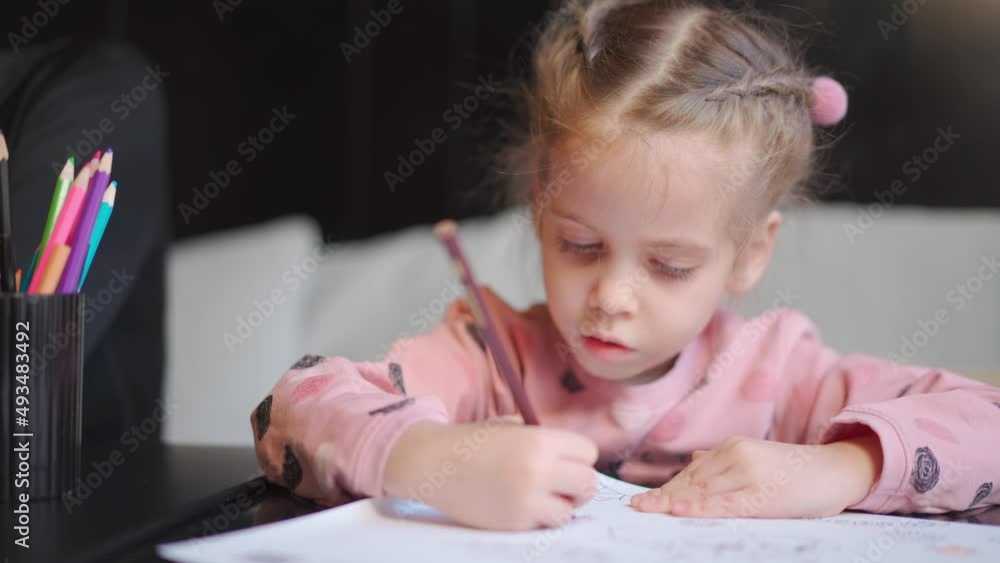 Child drawing sitting on table middle shoot. Caucasian female little girl draws with colored pencils. Female child doing homework portrait shoot Child drawing sitting on table middle shoot. Caucasian female little girl draws with colored pencils. Female child doing homework portrait shoot
