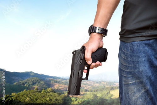 automatic 9mm pistol gun holding in right hand with blurr mountain and agricultural area background. concept for using pistol to protect properties and humans in crisis situations around the world.