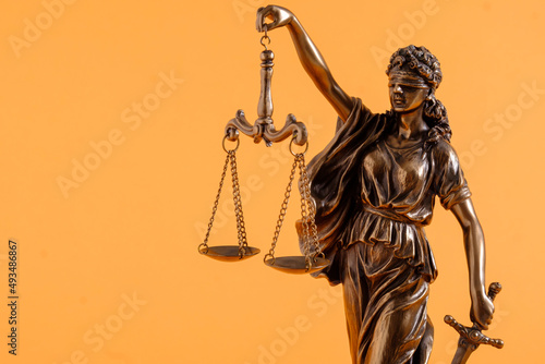 Figure of justice holding scales over orange photo