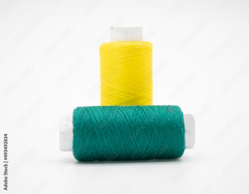 Sewing thread and bobbin in Dark Cyan and yellow on isolated white background Sewing thread and bobbin in Dark Cyan and yellow on isolated white background