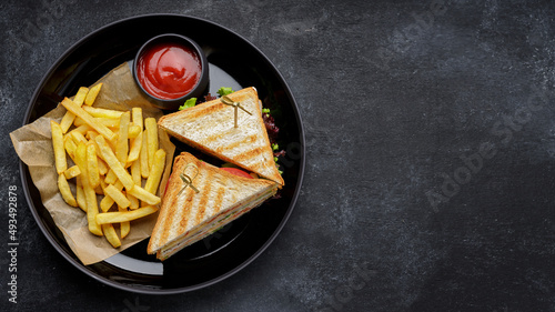 Sandwiches with ham, tomato and cheese and french fries, with space for text on a dark background