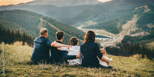 Family mom dad and 3 son boys sit on the grass and look at the mountains. © Александра Вишнева