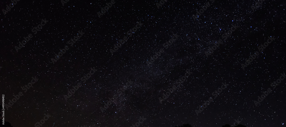 Obraz premium Panorama, blue night sky, milky way and stars on a dark background, universe filled with stars, nebula and galaxies with noise and photo pigmentation by long exposure and white balance selection focus
