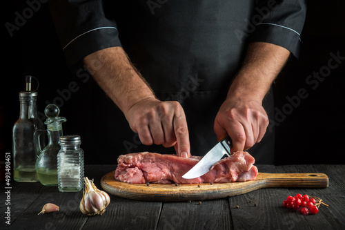 Professional cook cuts meat with a knife before baking. Spices on the kitchen table for preparing a delicious lunch