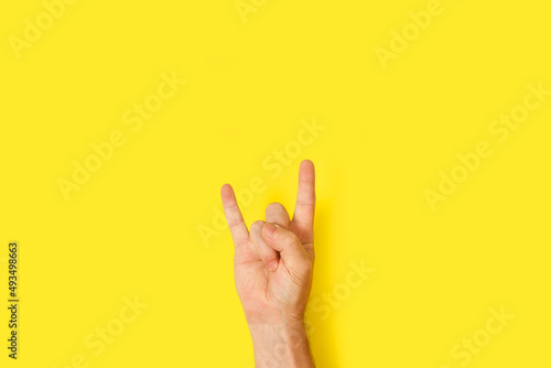 Mano con gesto seña de rock and roll sobre un fondo amarillo brillante liso y aislado. Vista de frente y de cerca. Copy space