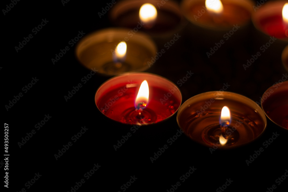 Round candles burn in dark. Wax candles on dark background. Red and yellow lights. Round candles burn in dark. Wax candles on dark background. Red and yellow lights.