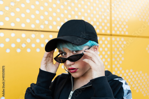 Portrait of a caucasian girl with a cap, short bluish hair and sunglasses looking at the camera photo