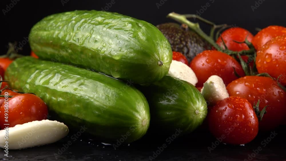Cherry tomatoes, cucumbers, garlic, avocado and red onion on a black background in water drops. Cherry tomatoes, cucumbers, garlic, avocado and red onion on a black background in water drops.