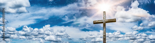 Religious background banner panorama - Old steel cross with blue sky, clouds and sunbeams