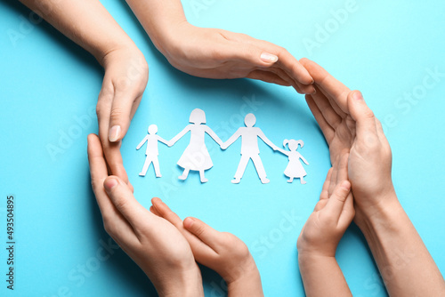Parents and child protecting paper cutout of family on light blue background, top view