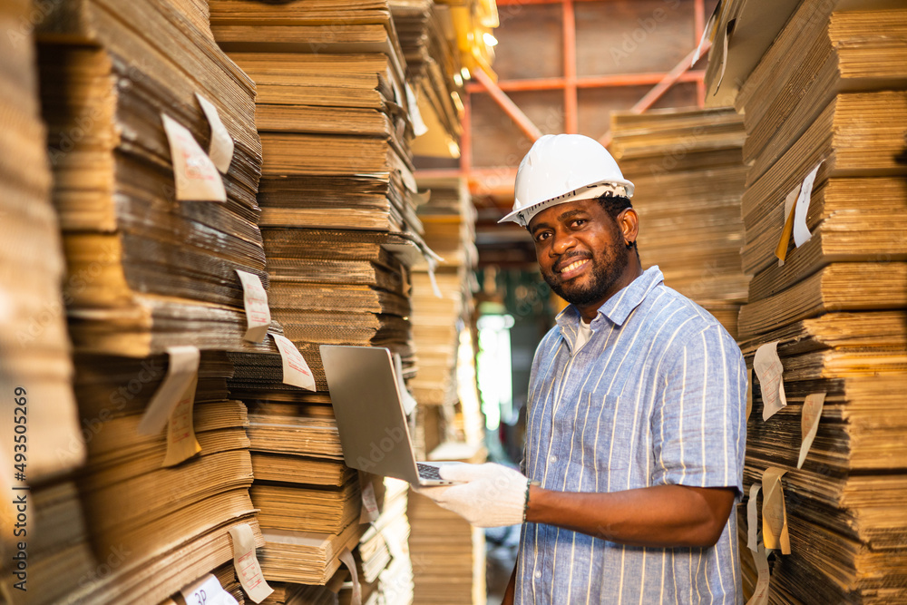 Happy male factory manager using digital tablet in warehouse while standing against goods shelf looking at camera.Products and corrugated cardboard. Small business factory concept.