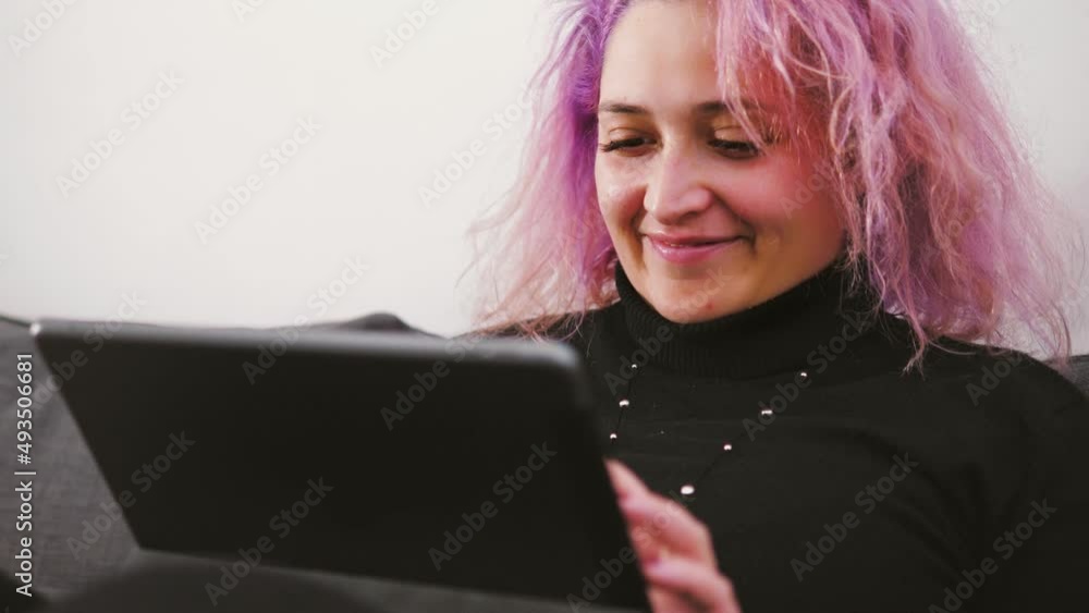 Young woman with pink hair is sitting on the sofa taking notes. Young woman with pink hair is sitting on the sofa taking notes.