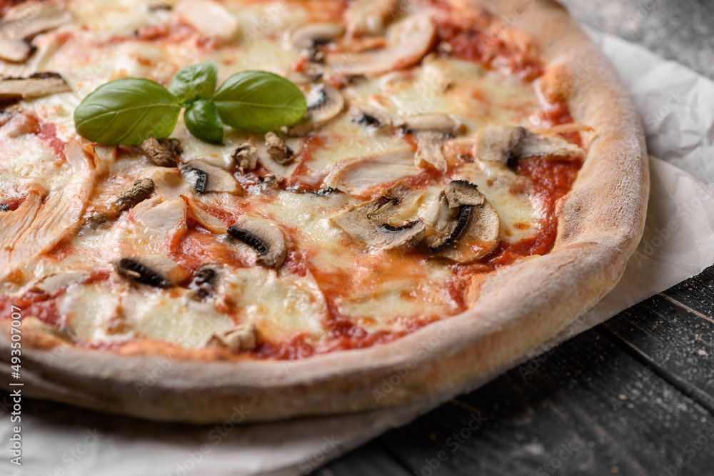 Freshly baked meat pizza. Appetizing pizza from whole grain dough with cheese, mushrooms and chicken meat. Served on parchment paper. Dark wooden background with sprinkled flour. Cropped image. Freshly baked meat pizza. Appetizing pizza from whole grain dough with cheese, mushrooms and chicken meat. Served on parchment paper. Dark wooden background with sprinkled flour. Cropped image.