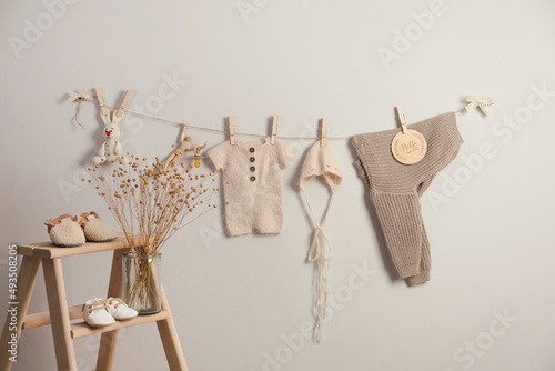 Baby clothes and accessories hanging on washing line near light grey wall
