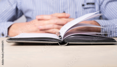 Man sitting at table with open planner. Crossed arms closeup. Man thinking about plans, important information, agenda. High quality photo