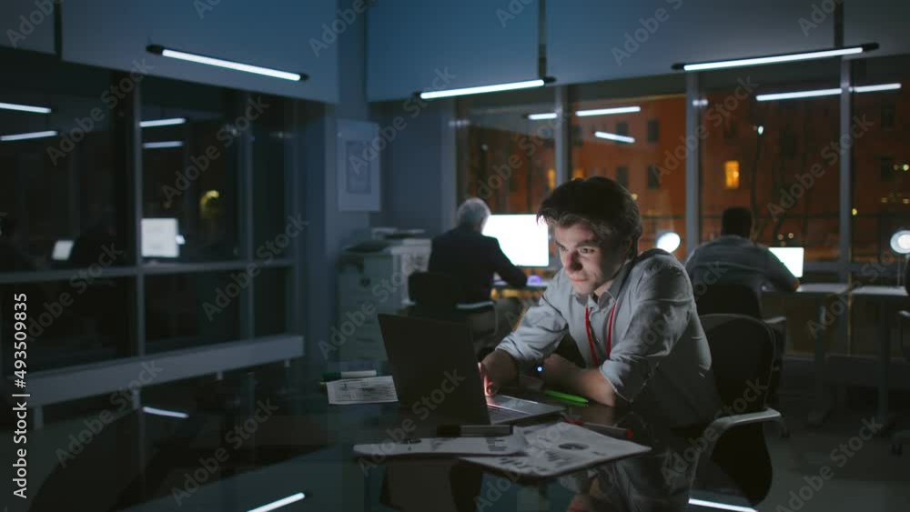 Portrait of happy businessman looking at laptop and laughing working late at night in modern office Portrait of happy businessman looking at laptop and laughing working late at night in modern office