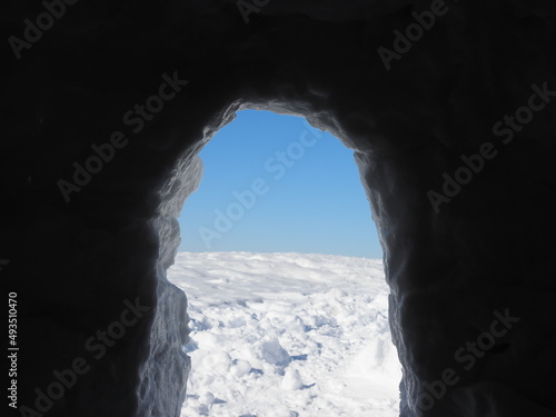 view from inside of a snow grotto into bright winter landscape in the austrian alps.