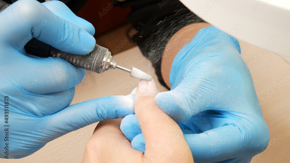 Manicurist in process of removing gel polish or acrylic from nails using manicure machine. Process of hardware manicure in the salon. Nail manicure process in a beauty salon. Nail beauty salon. Manicurist in process of removing gel polish or acrylic from nails using manicure machine. Process of hardware manicure in the salon. Nail manicure process in a beauty salon. Nail beauty salon.
