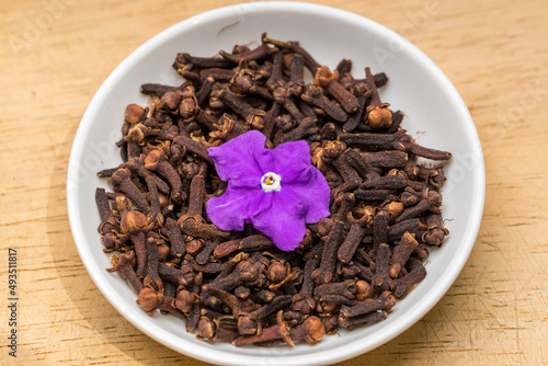 Cloves and pink flower in a white bowl on wooden table