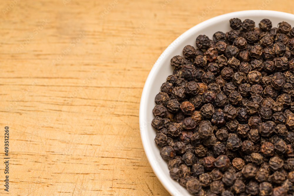Black pepper in a white bowl on wooden table Black pepper in a white bowl on wooden table