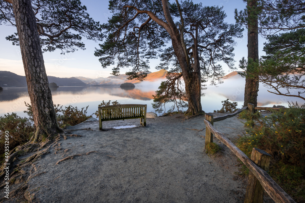 Lone wooden bench with peaceful view of misty lake on a fresh Winter morning. Friars Crag, Derwentwater, Lake District, UK.