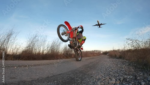 Professional extreme sportsman biker riding bike outdoors. Man does trial trick wheelie on motocross photo