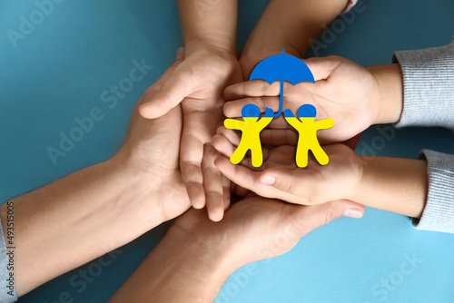 Wallpaper Mural Stop war in Ukraine. Family holding human shaped figures with colors of Ukrainian flag in hands on light blue background, top view Torontodigital.ca