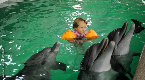 a little girl with dolphins swims in orange sleeves in clear water. High quality photo