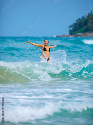 A young girl in a green bathing suit stands by the sea and laughs with her arms outstretched. High quality photo