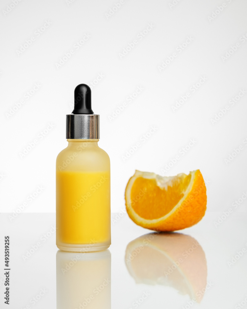 A bottle of vitamin C serum and slice of orange in the background with reflection. A bottle of vitamin C serum and slice of orange in the background with reflection.