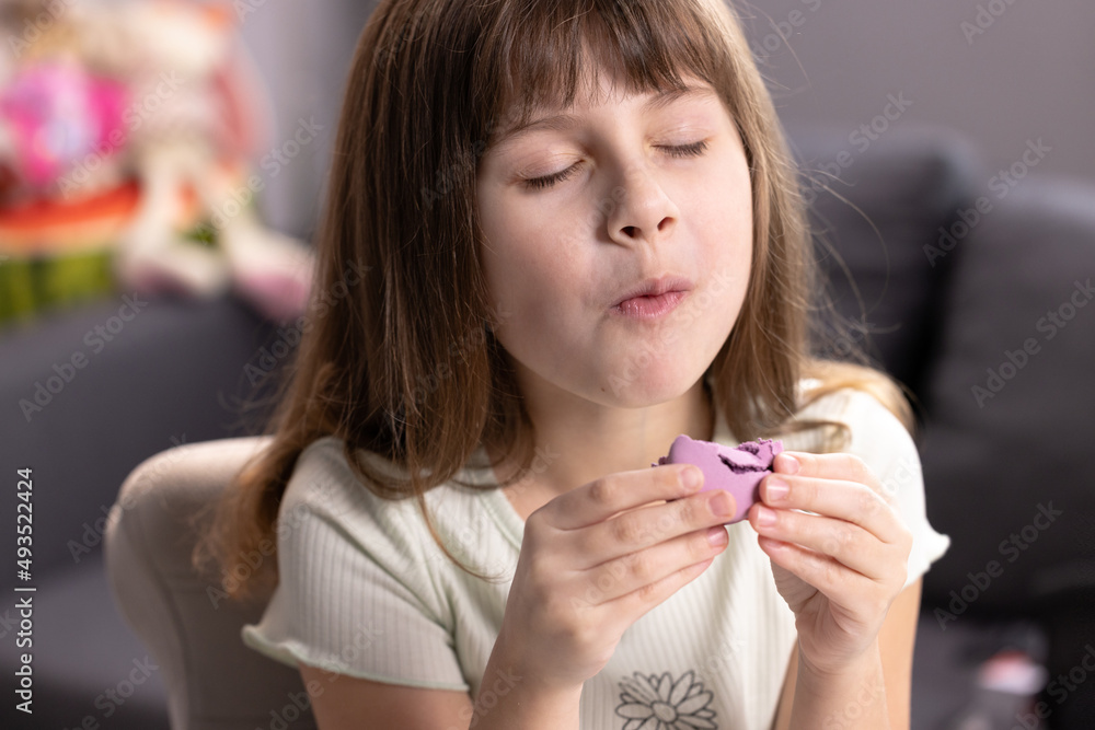 School girl on a home background, licks her lips, eating one violet macaron, closes her eyes with pleasure. Dessert person, sweet tooth, gourmet. Feeling good, delicious School girl on a home background, licks her lips, eating one violet macaron, closes her eyes with pleasure. Dessert person, sweet tooth, gourmet. Feeling good, delicious