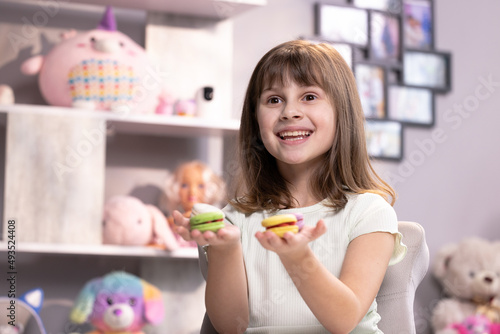 Attractive smiling cute school kid girl holds four tasty cookies in her hands and look at camera. Traditional French multicolored macaroon. Food concept