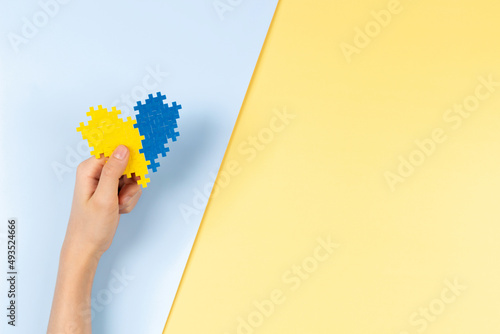 World Down syndrome day background. Child hands holding blue and yellow Down syndrome awareness day heart on pastel yellow and blue background. Top view, copy space