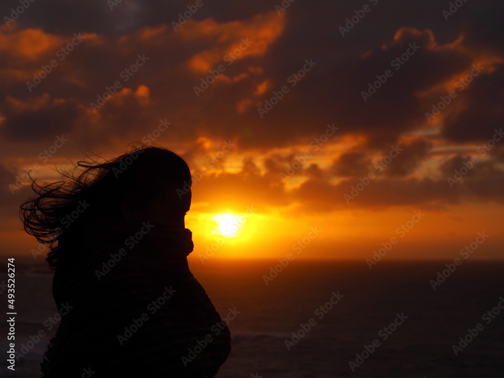A woman silhouette with the coast sunset in the background.