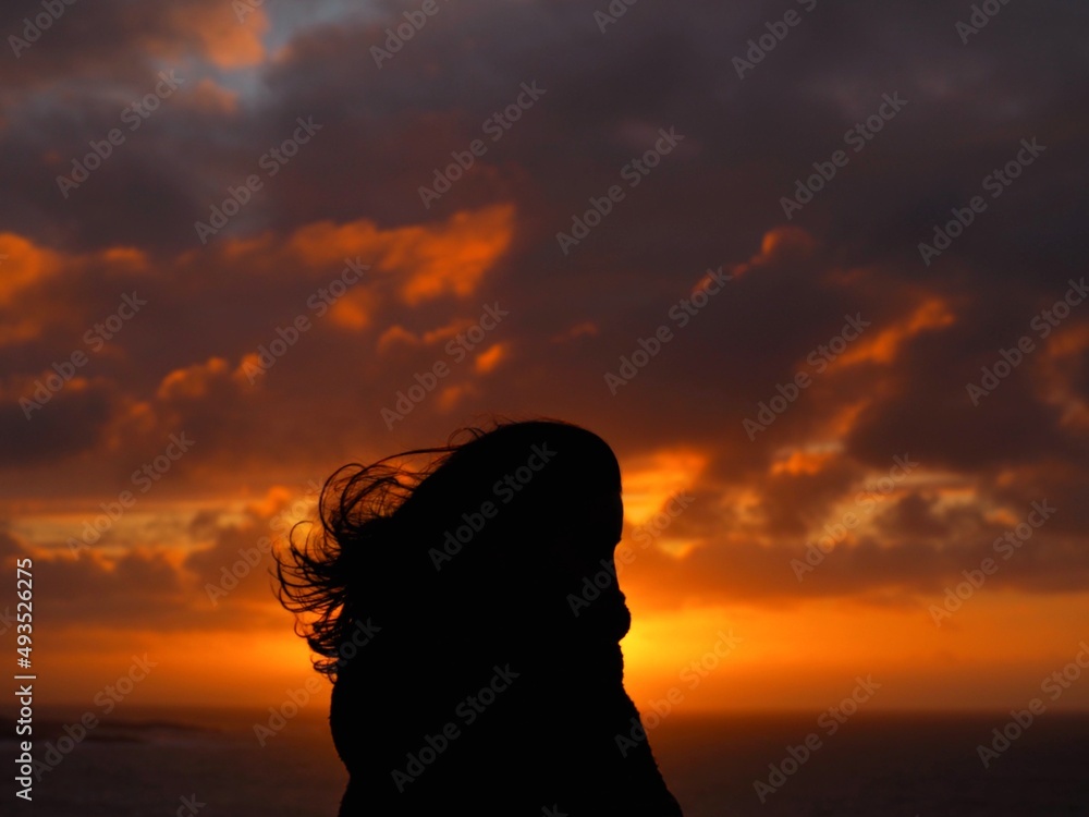 A woman silhouette with the coast sunset in the background.