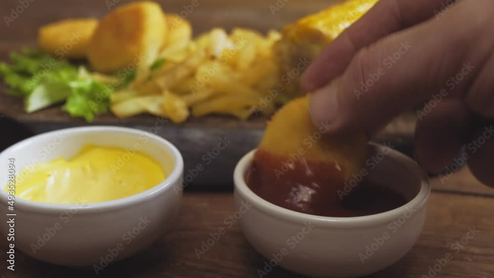 Hands take nuggets from the plank and dip them in ketchup Hands take nuggets from the plank and dip them in ketchup