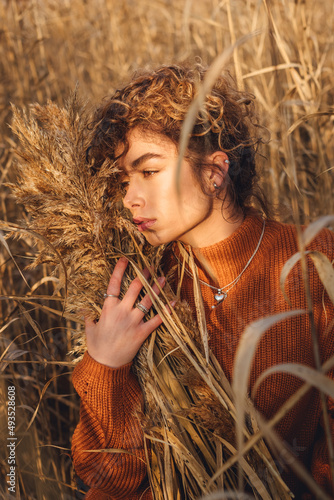 Portrait of beautiful young woman outdoor posing while holding a bouquet of reeds and feels emotional