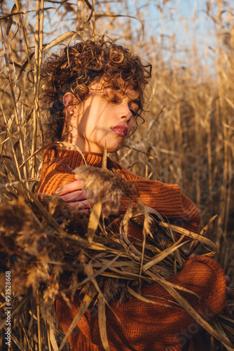 Portrait of beautiful young woman while posing outdoor and holds bouquet of reeds