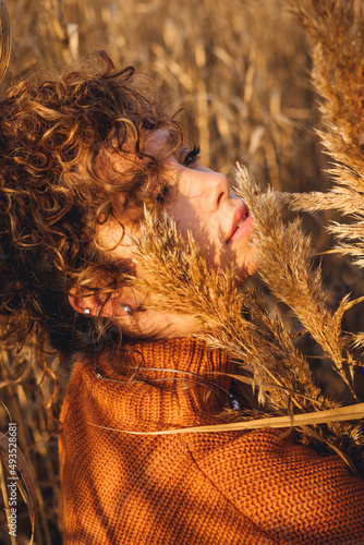Portrait of beautiful young woman while posing outdoor and holds bouquet of reeds