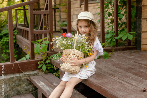 Billede på lærred Cute little girl sitting on doorstep of country house with basket of wildflowers