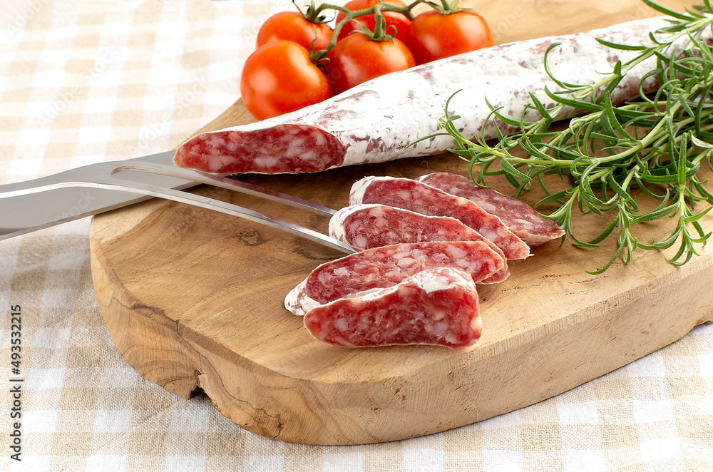 Traditional sausage cut into pieces with knife and fork with rosemary and spices on wooden cutting board on rustic background Traditional sausage cut into pieces with knife and fork with rosemary and spices on wooden cutting board on rustic background