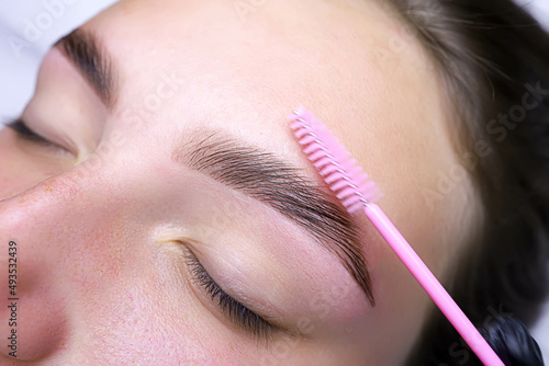 combing the hairs in the eyebrows with a brush after the procedure of coloring and laminating the eyebrows photo