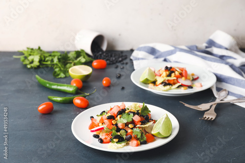 Plates of Mexican vegetable salad and ingredients on table