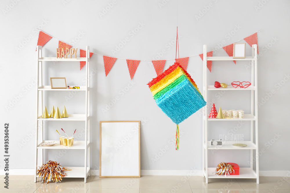 Interior of light room with hanging Mexican pinata and shelving units decorated for Birthday party