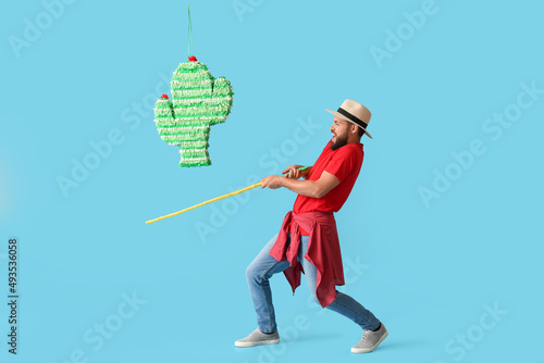 Handsome man breaking Mexican pinata on color background © Pixel-Shot