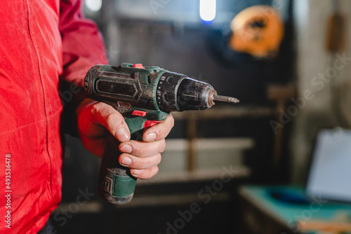 Electric screwdriver in hand of unknown caucasian man in dark workshop copy space
