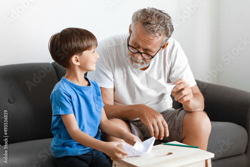Senior man and his little grandson with paper boats at home