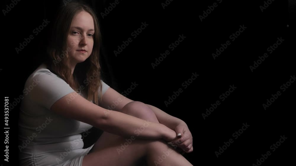 Long hair girl, white shirt and shorts sitting on the floor on black background. Keep calmness, qiuete, tranquility.